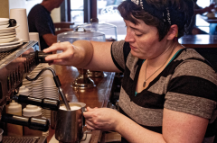 A woman steams milk in a coffee shop.