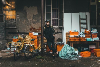 A man stands in an alley in front of grocery carts full of his life's possessions.