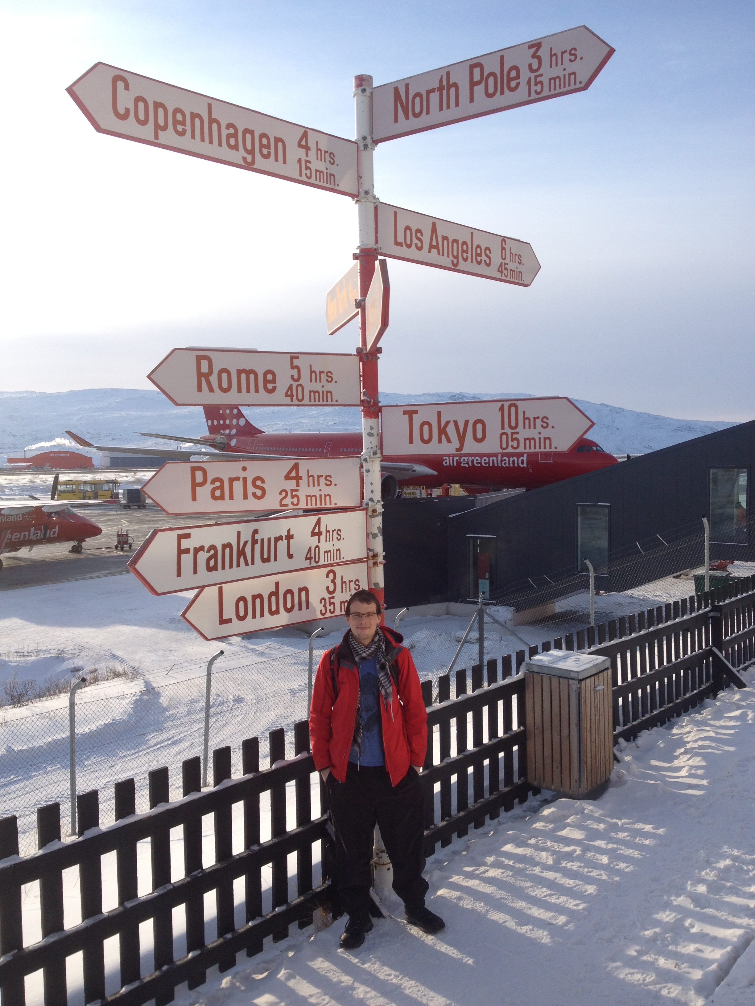 Carleton M.Sc. student Keegan Smith standing under the Kangerlussuaq airport signpost, north of the Arctic Circle.