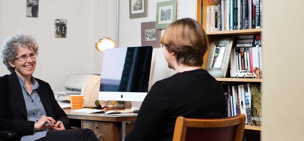 two women talking next to a computer desk