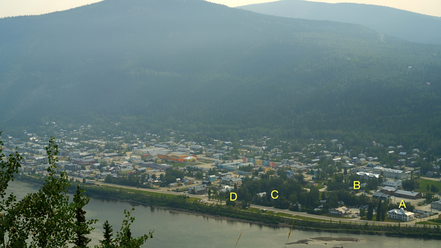 View of Dawson Vity from a hill across the river, showing a concentration of buildings on the river's edge with a mountain behind.