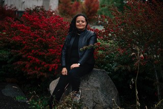 Dr. Qanita Lillaby sits on a boulder, surrounded by fall foliage.