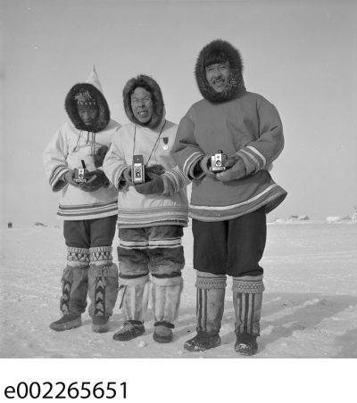 Black and white photo of three Inuit men holding cameras