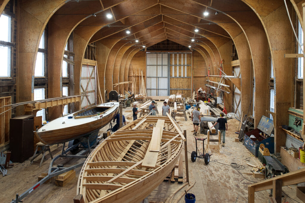 A spacious wooden shed interior holds a partially built boat.