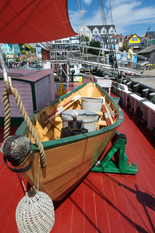 A small, bright yellow wooden boat sits on the bright red deck of a larger boat.