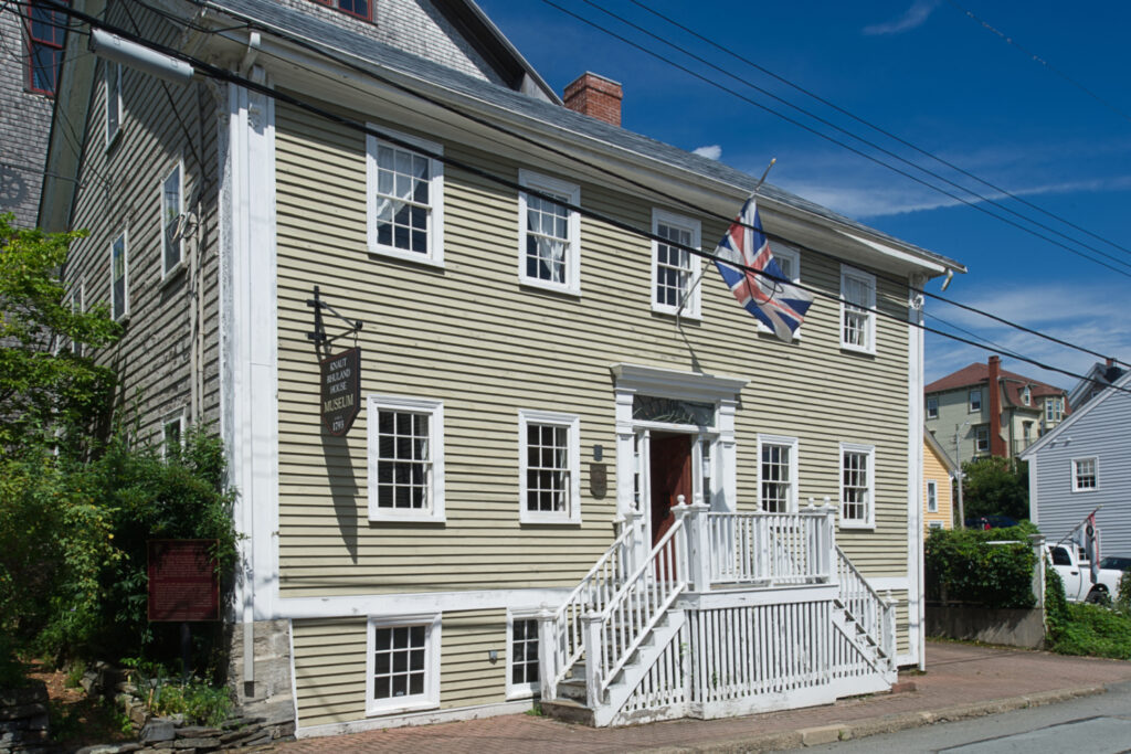 A simple, symmetrical tw-story wooden house, sheathed in clapboard.