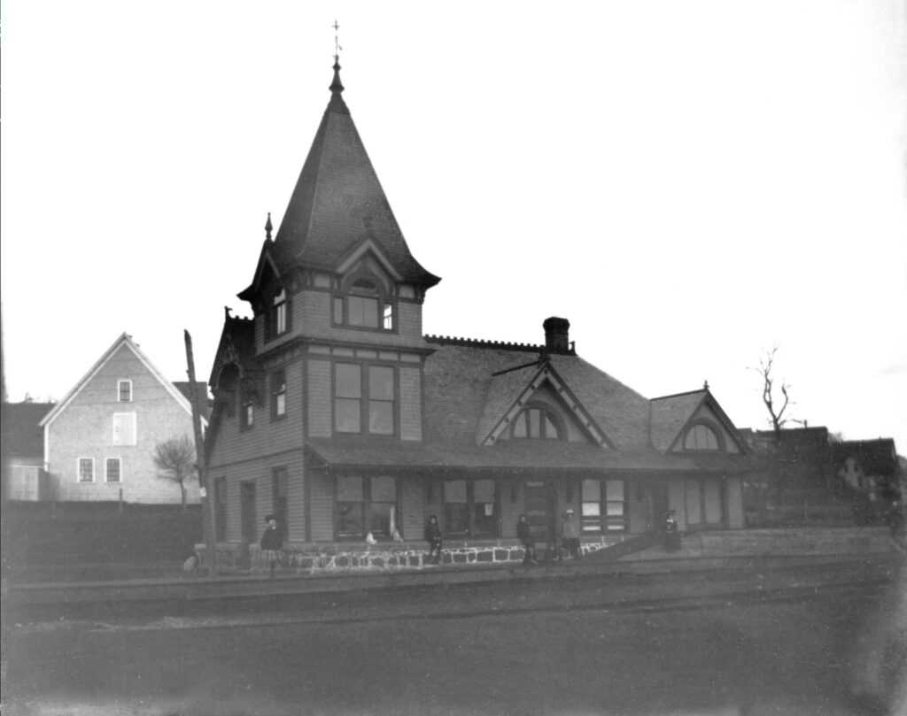 An archival photo of a picturesque wooden Victorian building, with several steep gables and a tall spire in one corner.