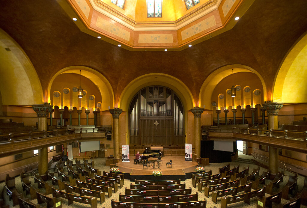 A lofty space beneath a dome, with chairs fanning out around a stage flanked by monumental arches.