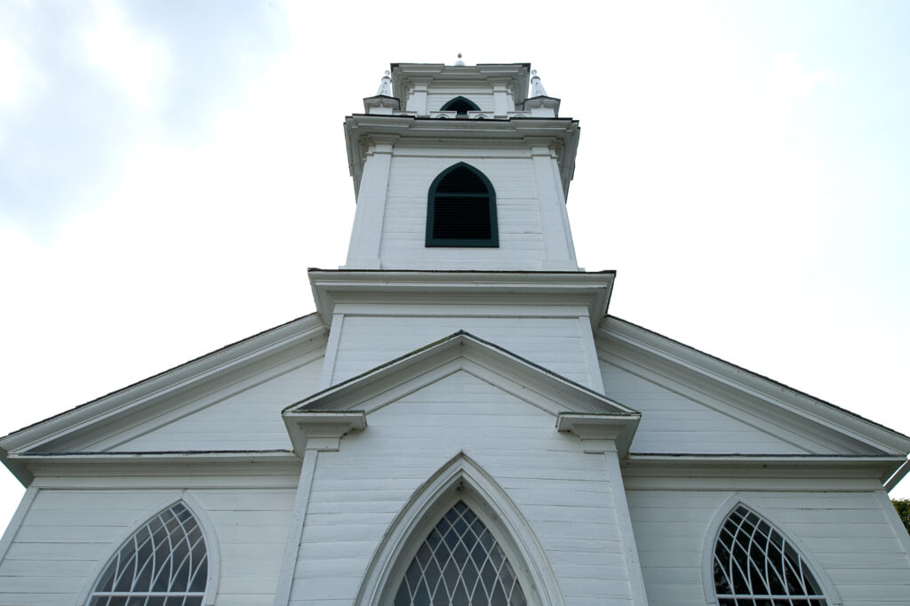 A layered wooden tchurch ower viewed from below at a steep angle rises toward the sky.