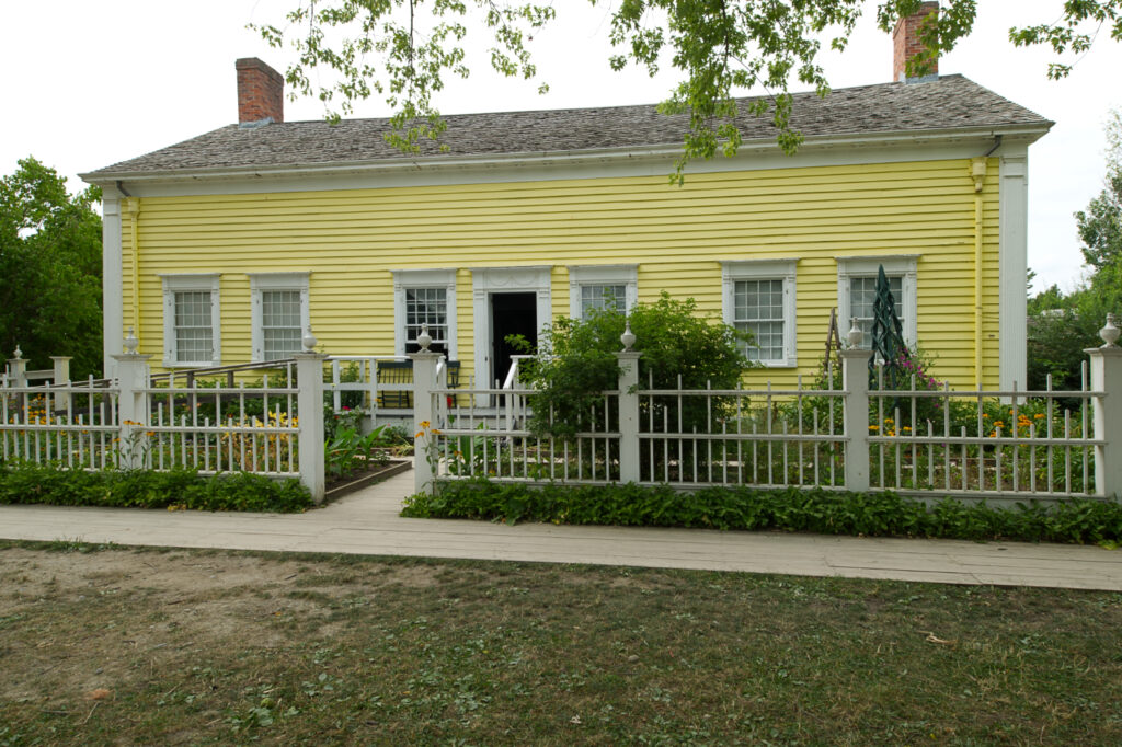 A wide, low, yellow wooden house, with a central door flanked by three symmetrical windows on each side.