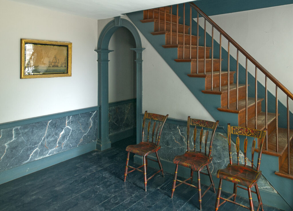 A semi-circular arch opens from the corner of a room with a staircase and three chairs on one side.