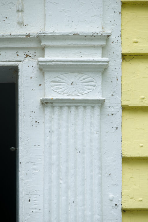 A detail of woodwork along the side of a door, with fluted pilasters and other decorative touches.