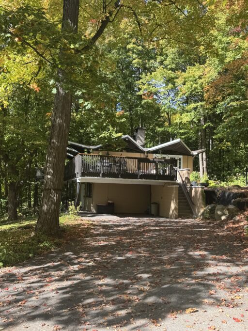 A modern house with a large 2nd-story veranda is surrounded by trees.