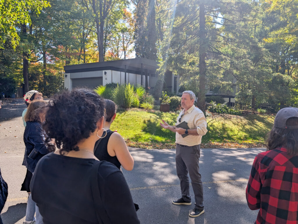 A group of students with a tour guide stand in front of a Modernist house.