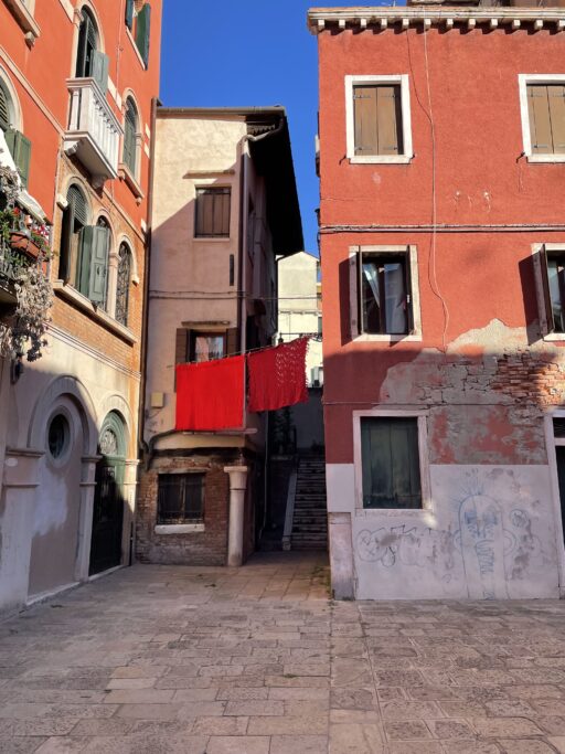 A cluster of brightly painted and clearly old stucco houses bridged by bright red laundry hanging on a line.
