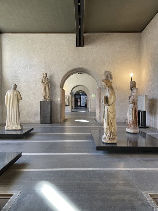 Several monumental statues on pedestals displayed in an austere interior with a series of receding arched doorways.