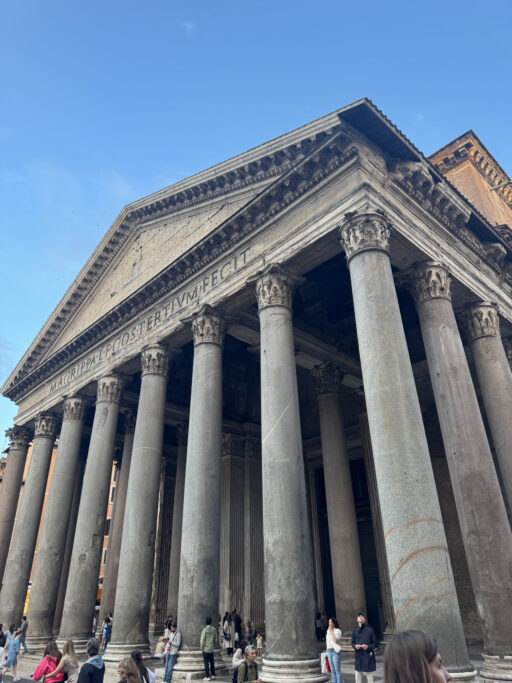 An immense temple façade qith smooth columns and Corinthian capitals towers above visitors.