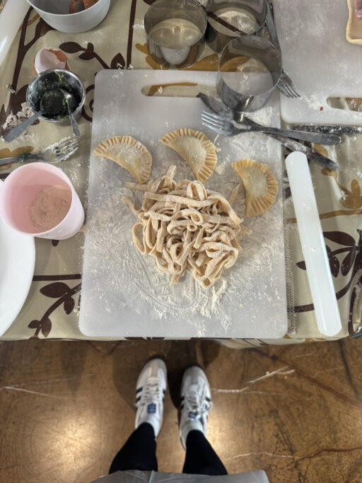 Overhead view of a cutting board sprinkled with flower beneath a jumble of freshly-made pasta.