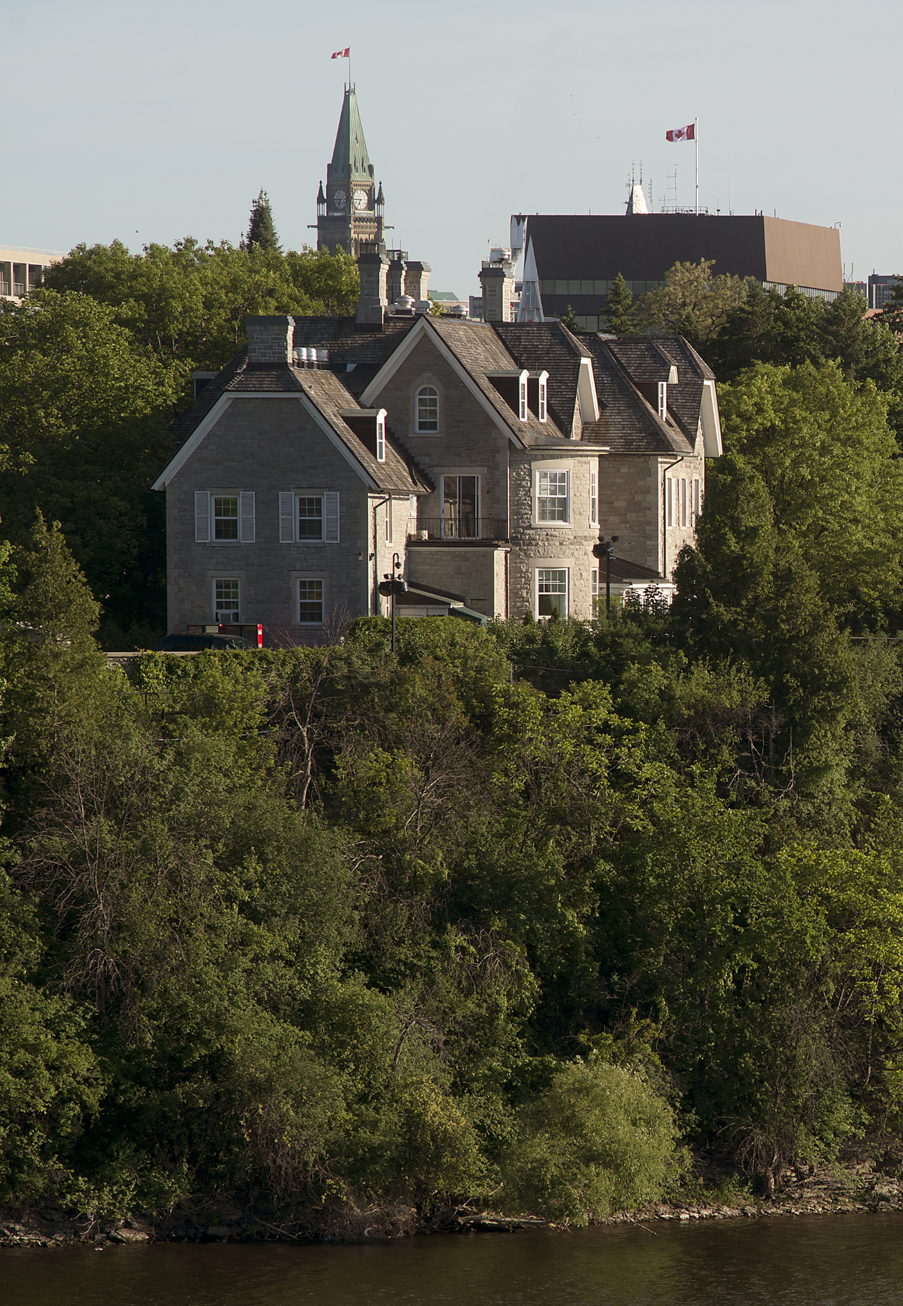 A large stone house sits on a cliff above a river.