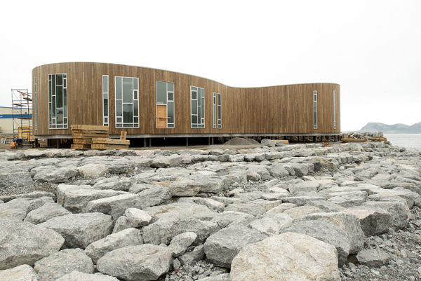 Curvilear wooden building on rocky landscape.