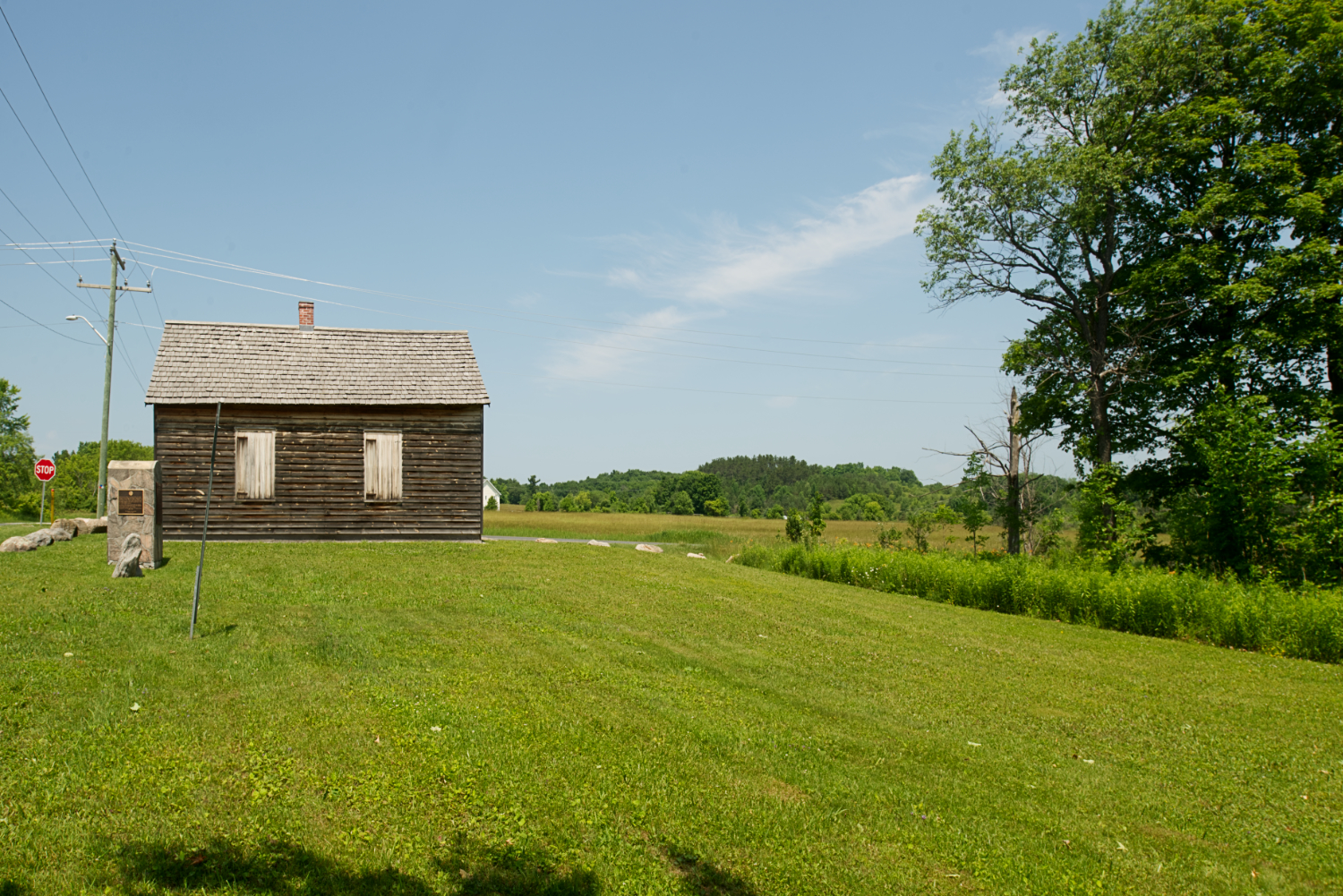 A broad, grassy field with a small log building at the far end.