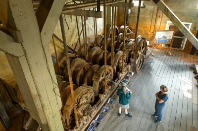 Viewed from above, two people look at the huge gears of the dredge machinery