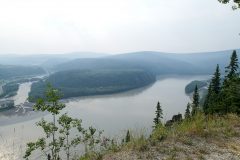 A wide river flows into the distance. There is a green, vegetation-filled point of land at its point of confluence with a second, smaller river.