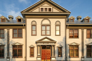 A Classical wooden facade with pilasters and a pediment over teh door.