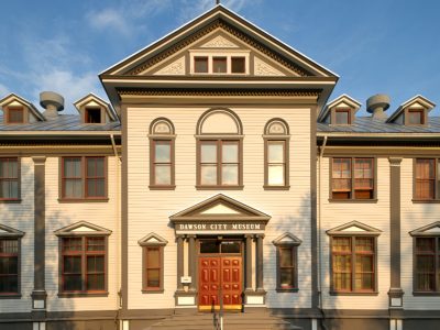 A Classical wooden facade with pilasters and a pediment over teh door.