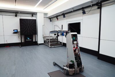 Human Performance Laboratory showing the GaitTronics SoloWalk system, force plates embedded in the floor, Dynavision D2 vision trainer and instrumented staircase in the background, and motion capture cameras along the border of the ceiling.