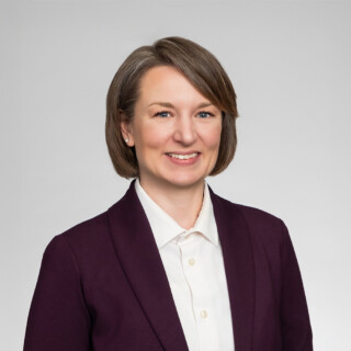 A professional headshot of a woman wearing a purple dress jacket and a white shirt.