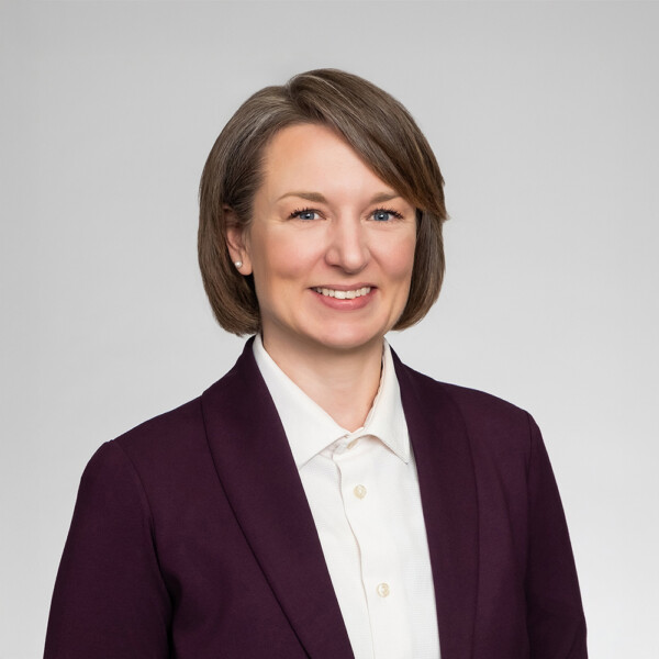 A professional headshot of a woman wearing a purple dress jacket and a white shirt.