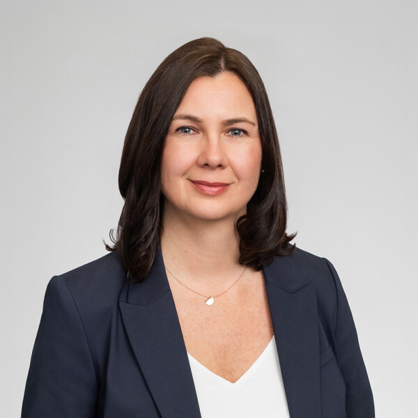 A professional headshot of a woman wearing a navy blue suit, and a white shirt.