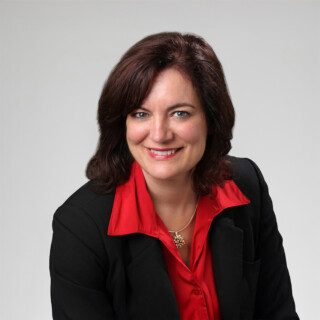 A professional headshot of a woman wearing a red dress shirt and a black dress coat.