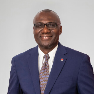 A man with glasses wearing a blue suit, poses for a professional headshot.
