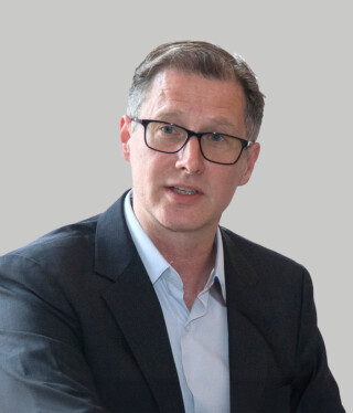 A professionally dressed man speaks into a microphone.