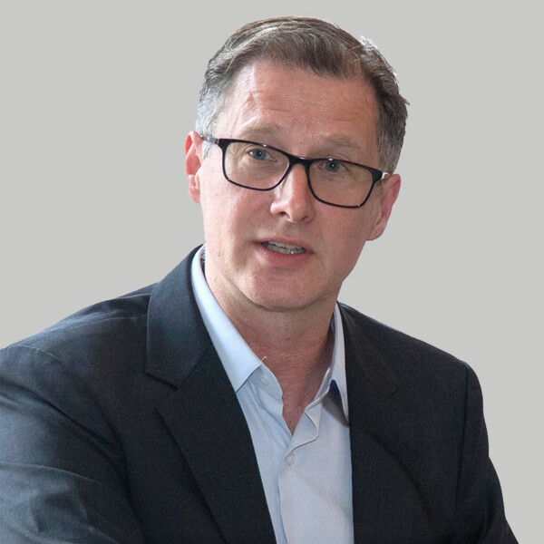 A professionally dressed man speaks into a microphone.