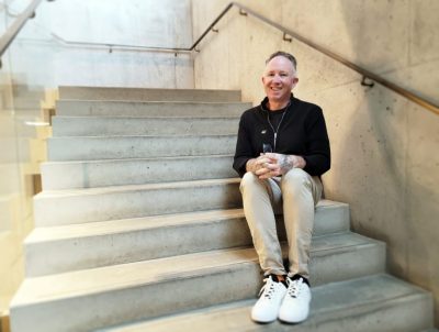 A middle-aged white man sits on a staircase, smiling.