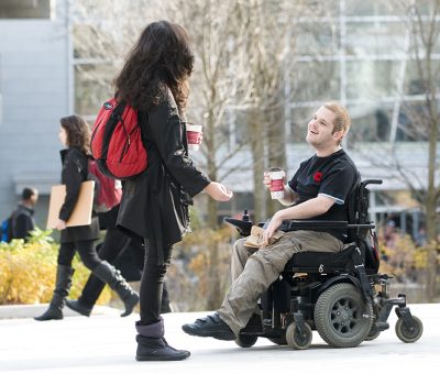 Two students, one using a mobility device, chatting in the courtyard outside the Carleton university centre