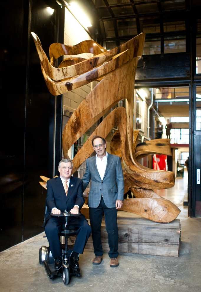 Lieutenant Governor David Onley, left, with sculptor David Fels posing in front of Fels' "Sailing Through Time" sculpture, a large curved, abstract shaped wooden sculpture.
