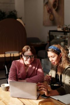 Two women sitting at a table, collaborating on a laptop. One of the women is in a wheelchair.