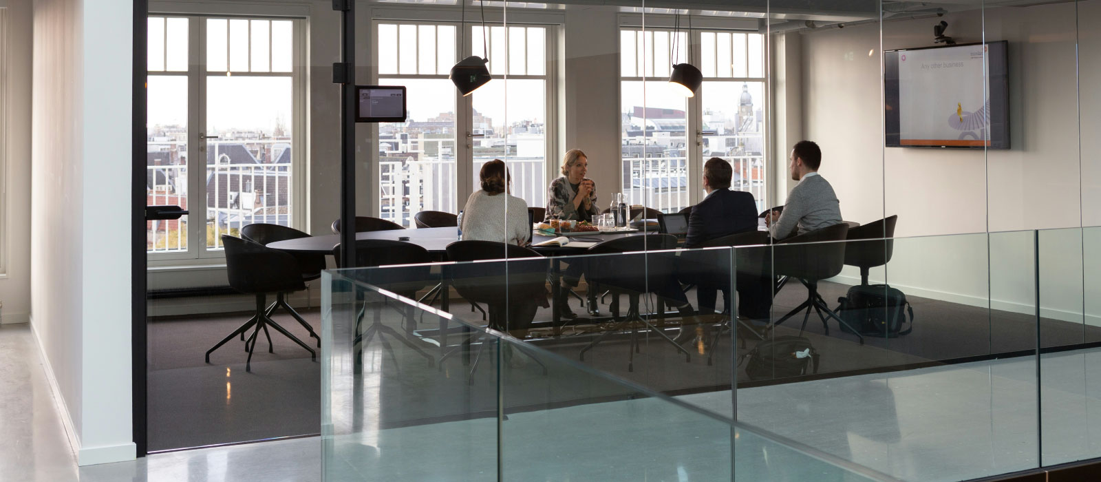 A meeting between four indiviudals in a conference room with glass walls.