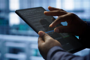A man holds a tablet in one hand while navigating the screen with the other. His finger and thumb are positioned in a pinch gesture as he selects a line of code for review on the screen.