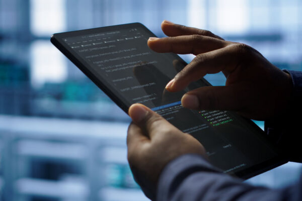 A man holds a tablet in one hand while navigating the screen with the other. His finger and thumb are positioned in a pinch gesture as he selects a line of code for review on the screen.