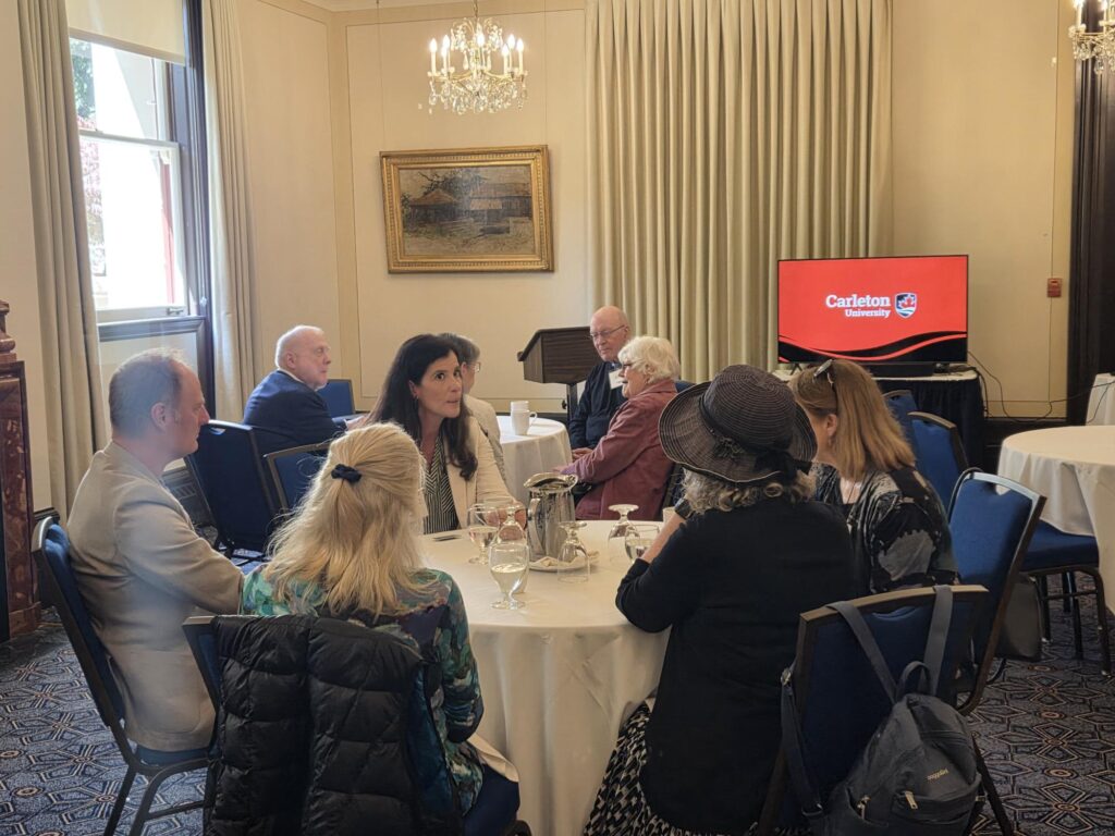 photo of 5 people sitting around a round table inside a hotel conference room.