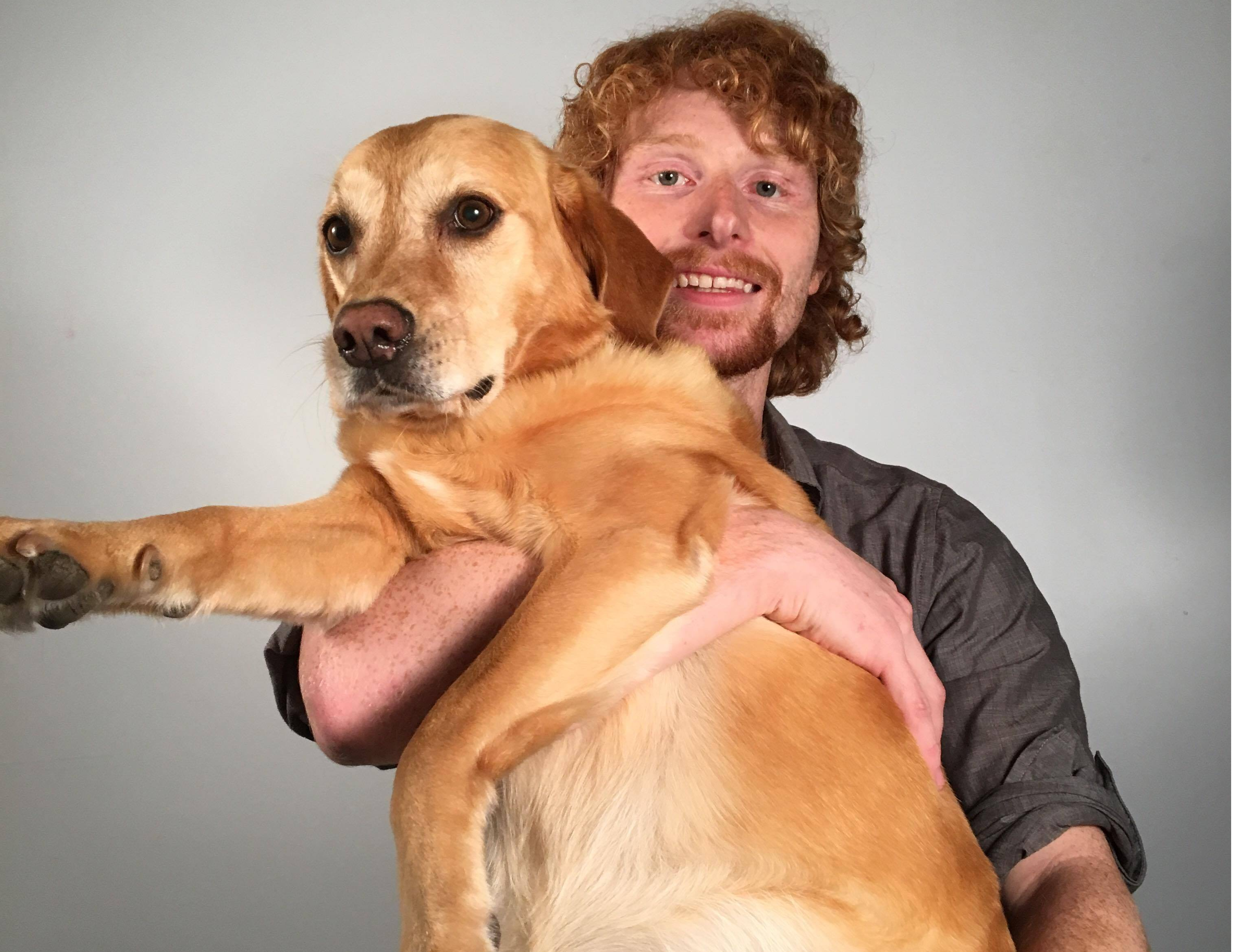 A photo of the author, a young light-skinned man with orange hair, holding a dog.