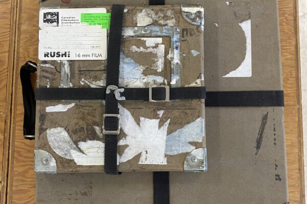 Two 16mm film shipping boxes stacked on top of a wooden table.