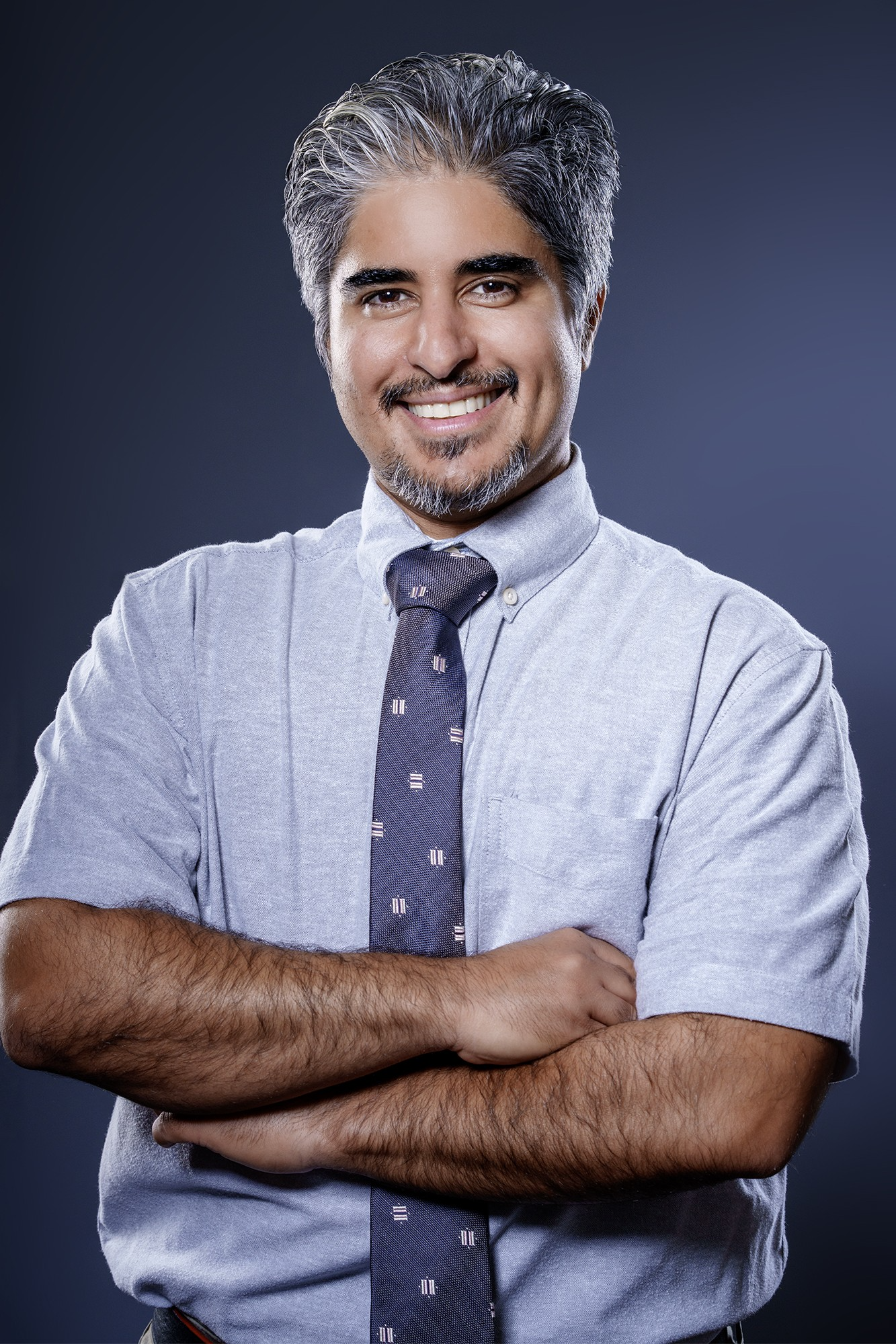Contract Instructor Yaldah Azimi, posing with crossed arms wearing a grey shirt with a dark grey tie.