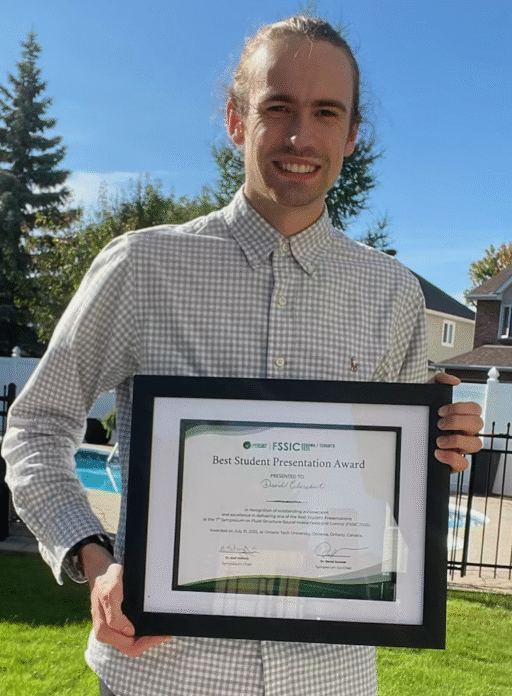 photo of David Clarabut holding his framed award certificate. He is wearing a checkered button up shirt.