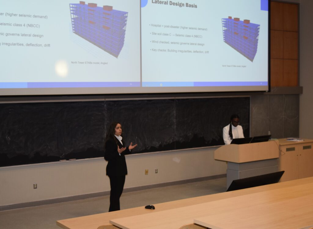 Photo shows Armita Ghannadbashi & Nimi Tella presenting their project in front of a lecture hall in formal clothing.